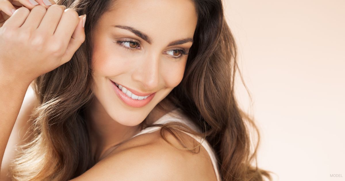 Woman with long wavy hair smiling and looking to the side. (Model)