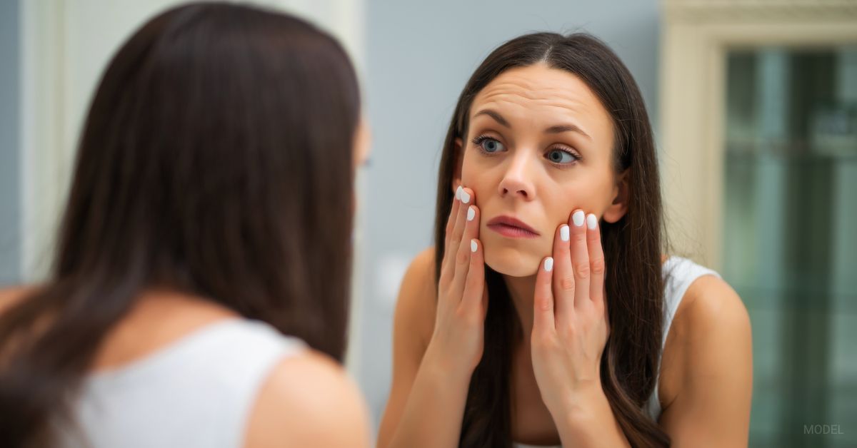 woman standing in mirror looking at her Ozempic face (Model)