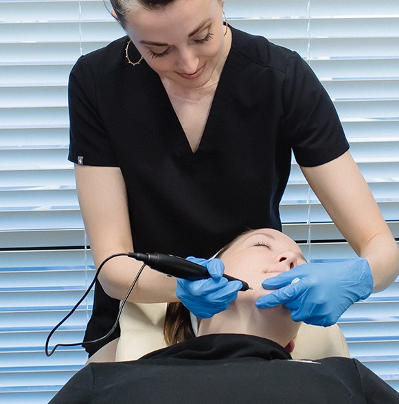 woman holding black plasma pen over womans jowls