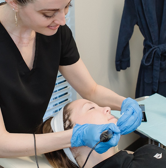 Woman holding black plasma pen over womans jowl treating sagging skin.