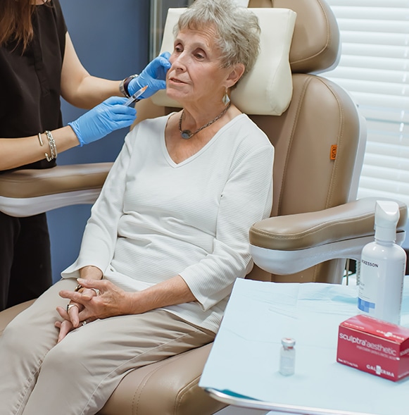 Older woman sitting in chair being treated with Sculptra