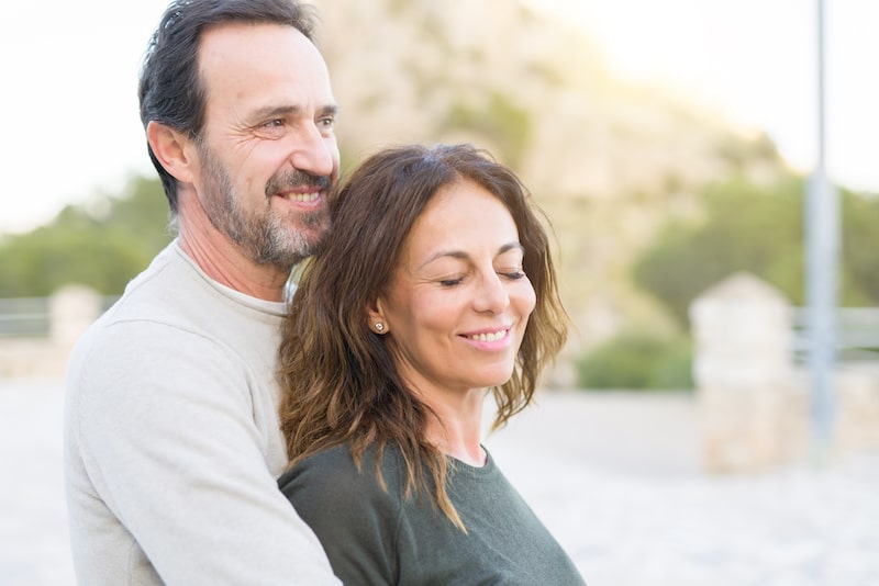 Attractive middle aged man holding his beautiful partner at a park while smiles