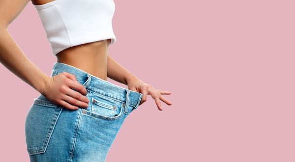 Image of a woman demonstrating her weight loss in a too-large pair of jeans